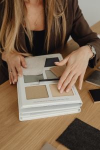 Kaboompics - Woman Layering Neutral Fabric Swatches Over Material Sample Catalog