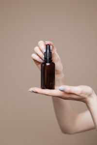 Kaboompics - Hand Lifting Amber Dropper Bottle Against Beige Studio Background, Minimal Aromatherapy Image