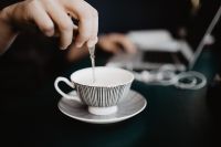 Kaboompics - Close-Up of Spoon Stirring Coffee in a Striped Cup with Laptop in Background