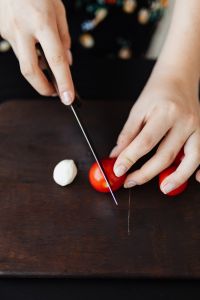Kaboompics - Close-Up of Hands Cutting a Tomato on a Dark Board with Copy Space