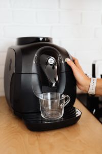Hand Pressing the Button on a Black Espresso Machine in a Bright Kitchen