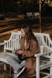 Kaboompics - Woman Sitting on a White Park Bench with Coffee and Smartphone