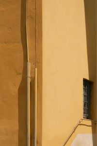 Kaboompics - Yellow Stucco Building Facade with Pipes and Barred Window, Italy
