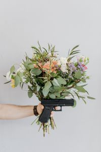 Kaboompics - Mixed Flower Bouquet above a Black Handgun Prop against a Pale Studio Wall