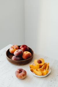 Kaboompics - Peaches in Wooden Bowl with Sliced Fruit on Minimal Light Background