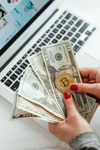 Kaboompics - Hand Holding Bitcoin Coin and Dollar Bills by Laptop
