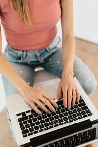 Kaboompics - Close-Up of Woman Typing on a Laptop in a Pink Top and Light Denim, Remote Work Content