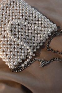 Kaboompics - Close-Up Pearl Beaded Evening Bag with Dark Chain on a Taupe Surface