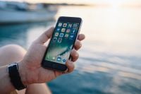 Kaboompics - Hand Holding a Smartphone with App Icons Against a Blurred Marina