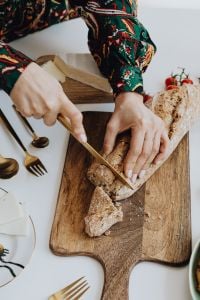 Kaboompics - Woman Slicing Rustic Bread on a Wooden Cutting Board