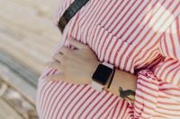 Kaboompics - Close-Up Pregnant Belly, Hand and Smartwatch in Striped Dress