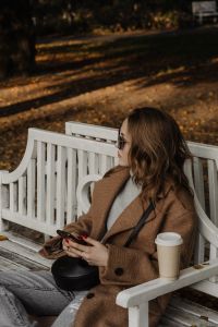 Kaboompics - Woman in Sunglasses Sitting with Coffee on a White Park Bench