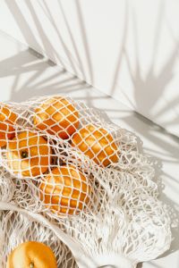 Kaboompics - Vertical Close-Up of Oranges in a Mesh Produce Bag with Sunlit Shadows