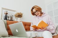 Kaboompics - Woman Reading Orange Notebook Beside Laptop