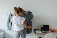 Kaboompics - Teen Girl Browsing a Clothing Rack with Black Floral Dress, Bedroom Outfit Selection