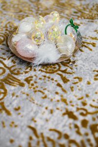 Kaboompics - Decorative Bowl of Pastel Glass Easter Eggs and Feathers on Gold-Patterned Fabric