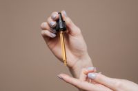 Kaboompics - Amber Dropper Raised by Hand Against Taupe, Minimal Skincare Product Background