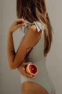 Kaboompics - Woman in Striped One-Piece Swimsuit Holding Grapefruit Behind Her Back