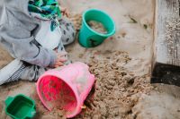 Kaboompics - Toddler Sitting in an Outdoor Sandbox with Pink and Green Buckets