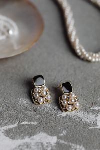 Kaboompics - Gold Drop Earrings with Black Square Stones and Pearl Accents on Concrete