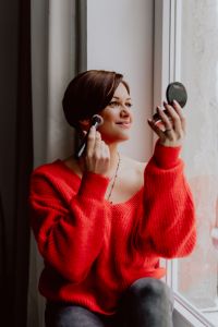 A woman in a red sweater does her make-up - applies a foundation with a brush