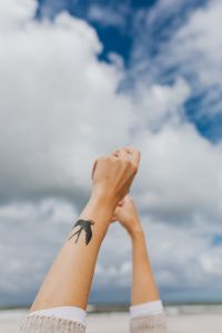 Kaboompics - Woman's Raised Arms and Swallow Tattoo Against Clouds, Minimal Freedom Concept Photo