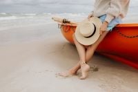 Kaboompics - Seaside Summer Lifestyle with Woman Sitting Beside an Orange Kayak and Straw Hat