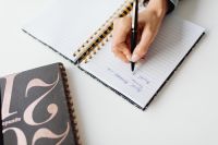 Kaboompics - Close-Up of Hand Writing in a Spiral Notebook Beside a Magazine