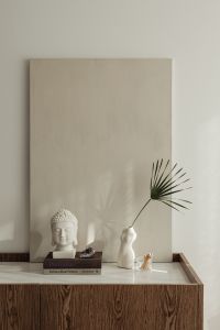 Kaboompics - White Buddha Bust, Palm Leaf Torso Vase, and Books On Wooden Console