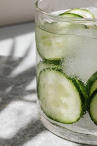 Kaboompics - Vertical Close-Up of Cucumber Slices in Iced Water, Condensation on Glass and Sunlit Marble Background