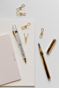 Kaboompics - Silver Fountain Pen with Gold Nib and Paper Clips on a Notebook beside a Pink Notepad