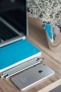 Kaboompics - Silver iPhone with a blue notebook, pencils and a plant