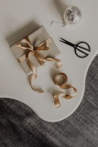 Kaboompics - Beige Christmas Present with Champagne Ribbon, Scissors and Pinecone on White Tray