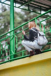 Kaboompics - Blonde woman in a black jacket and ripped jeans by a green handrail