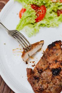 Kaboompics - Pork Neck Steak and Fresh Tomato-Lettuce Salad on White Plate with Fork
