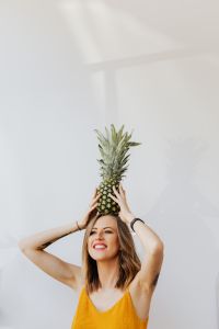 Kaboompics - Pineapple Crown above Smiling Woman’s Head with Raised Arms, Fresh Summer Portrait