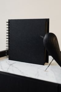 Kaboompics - Black Spiral Notebook with Sculptural Wooden Bird and Copy Space, Minimalist Desk Decor