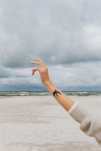 Open Hand Over a Wide Sandy Beach and Sea, Cloudy Coastal Background for Travel Design