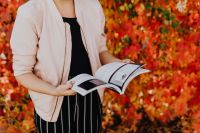 Kaboompics - Woman in a Beige Jacket Holding Open a Conference Book against Red Autumn Leaves