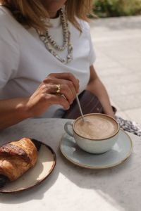 Kaboompics - Woman Stirring Cappuccino with Croissant at an Outdoor Cafe