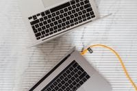 Kaboompics - Two Silver Laptops with Curved Orange Cable on White Textured Table