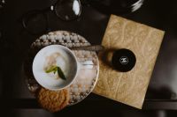 Kaboompics - Overhead Ornate Coffee Cup Still Life with Mint, Cookie, Eyeglasses and Gold Notebook