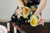Kaboompics - Close-Up of Hands Holding Two Avocado Halves over a Cutting Board