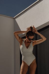 Kaboompics - Woman in Striped Swimsuit Tying Her Hair against a White Wall