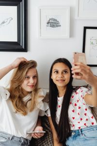Kaboompics - Teen Girl Holding a Phone for a Selfie with Her Friend on a White Couch