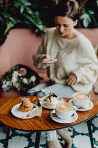 Kaboompics - Woman Browsing Her Phone at a Pink Cafe Bench with Lattes and Pastries