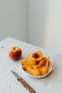Kaboompics - Peach Slices on White Plate with Whole Fruit and Neutral Copy Space
