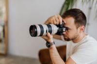 Kaboompics - Photographer Using a DSLR Camera with White Telephoto Lens in an Indoor Home Photography Workspace