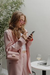 Kaboompics - Woman in Pink Suit Using Smartphone Beside Wine and Laptop