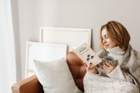 Kaboompics - Smiling Woman Reading on Sofa with a Cup of Tea